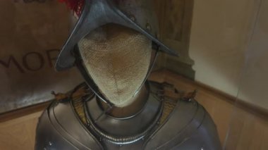 Müzede sergilenen kırmızı tüylü ortaçağ zırh kaskının yakın çekimi, tarihi Avrupa şövalyesi koruyucu donanımı ve kültürel mirasını gözler önüne seriyor.