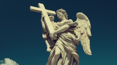 Mavi gökyüzüne karşı haç tutan mermer melek heykeli ruhaniliği, bağlılığı ve tarihi dini sanatı temsil eden klasik Hristiyan heykeli.