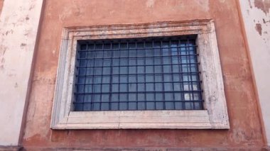 Vatikan 'ın yıpranmış turuncu duvarına taş çerçeveli ve tarihi karakterli parmaklıklar ardında yakın plan.