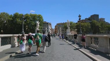 Roma, İtalya, 30 Temmuz 2025 - Turistler ve hacılar açık bir yaz gökyüzü altında Ponte SantAngelo 'da tarihi binalara doğru yürüyorlar.