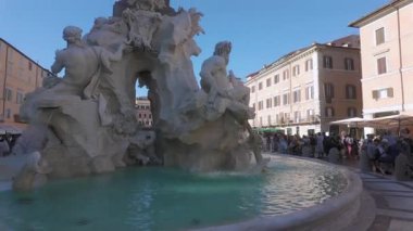 Roma, İtalya, 29 Temmuz 2025 - Navona Meydanı 'ndaki Dört Nehir Pınarı' nda mermer heykeller ve yakınlardaki tarihi binaları yansıtan su ve hareketli meydan