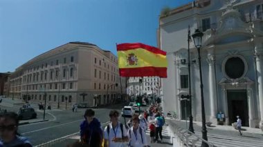 Roma, İtalya, 30 Temmuz 2025 - İspanyol bayrağı taşıyan genç bir grup turistle birlikte Barok kilisesi girişinde yürüyordu