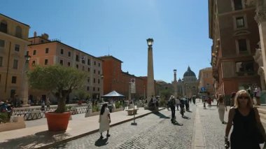 Roma, İtalya, 30 Temmuz 2025 - Arka planda Aziz Peters Bazilikası kubbesi bulunan Vatikan 'a giden kaldırım taşı caddesinde yürüyen ve scooter kullanan insanlar.