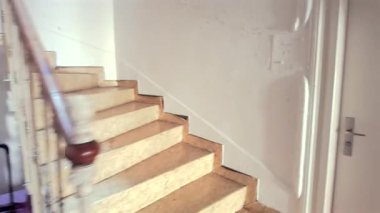 Bakış açısı, ahşap korkuluklu ve beyaz duvarlı iç merdiven, geçişi, yalnızlığı veya günlük olağan hareketleri çağrıştırıyor.