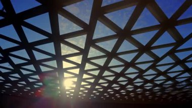 Parlak mavi gökyüzü ve güneş ışığına karşı üçgen desenli geometrik şebeke çatısı, soyut kentsel tasarım perspektifi yaratan mimari yapı