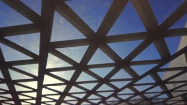 Geometrik çatı ızgarası. Güneş ışığı mavi gökyüzüne karşı üçgen açılardan gözetliyor. Mimari çizgiler ve kentsel tasarım vurgulanıyor.