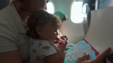 Anne ve küçük çocuk uçuşta birlikte renkli kitaplar okuyorlar. Ekonomi sınıfında pencere kenarında otururken hem meşgul hem de odaklanmış durumdalar.