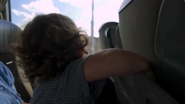 Kucağında oturan bebek yolculuk sırasında otobüs koltuğunun arkasındaki plastik tepsiyi açar ve keşfeder. Gezerken dokunaklı keşifler yapar.