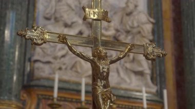 Üzerinde İsa 'nın figürü ve INRI yazısıyla altın haçın yakın plan, tarihi Avrupa kilisesinin arka planında mermer kabartması var.