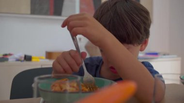 Yemek masasında çatalla spagettiyi karıştıran genç bir çocuk. Makarnayı hazırlarken kısmen yüzünü kollarıyla kapatıyor.