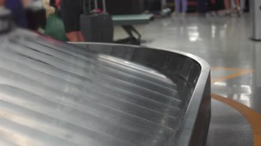 Havaalanı terminalinde bagaj atlıkarıncasında bavullar ve arka planda bekleyen gezginler.