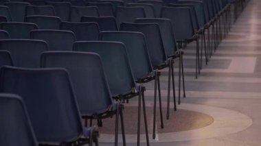 Toplantı, sunum ya da resmi etkinlik için kurulmuş büyük salondaki döşeme boyunca dizilmiş sıralı boş mavi sandalyeler.