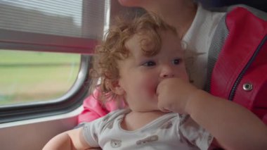 Yürüyen çocuk, anne kucağında dinleniyor, başını arkaya yaslıyor ve gündüzleri pencereden dışarı bakarken parmaklarını ağzına sokuyor..