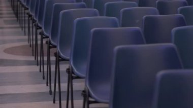 Boş mavi sandalyelerin simetrik sıraları halka açık toplantı ya da konferans için hazırlanmış geniş kapalı mekandaki desenli katlara dizilmiş.