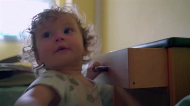 Kıvırcık saçlı çocuğun komodinin çekmecesini açması, yatak odasındaki mobilyaları merakla araştırması...