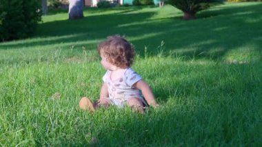 Küçük çocuk uzun yeşil çimenlerde sürünüyor, elleri ve dizleri aşağıda, güneşli bir günde açık parkı keşfediyor neşeli bir merak ve hareketle.