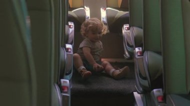 Yeni yürümeye başlayan çocuk, seyahat molasında yolcu koltuklarıyla çevriliyken ayakkabısını düzeltirken boş tur otobüsünde koridorda oturuyor.