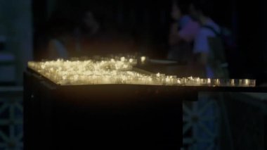 Kilisenin iç kısımlarında parlayan adak mumları dizisi, ziyaretçilerin bulanık arkaplanından önce sıcak bir yansıma ve dua atmosferi yaratıyor.