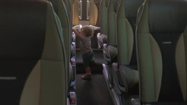 Boş tur otobüsünün koridorunda duran çocuk, seyahat durağı sırasında koltuklar arasında merakla keşif yapıyor.