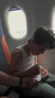 Uçakta oturmuş suşi yiyen genç bir çocuk gündüz uçuşu sırasında pencereden dışarı bakıyor. Sıradan bir aile seyahati anı.