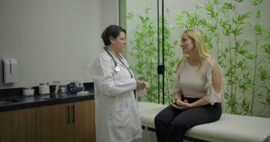 Tıbbi klinikte muayene masasında oturan orta yaşlı kadın hastaya bambu bitkisiyle danışmanlık yapan kadın doktor.