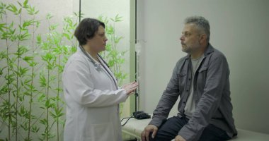 Klinikte tıbbi danışmanlık sırasında zor durumda olan orta yaşlı erkek hastaya destek veren kadın doktor