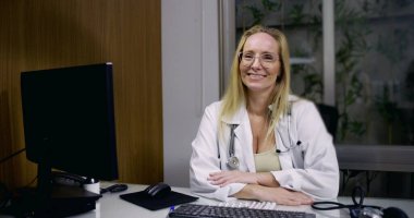 Modern klinikteki masasında güvenle gülümseyen kadın doktor hasta danışmanlığı ve profesyonel tıbbi araba için hazır.