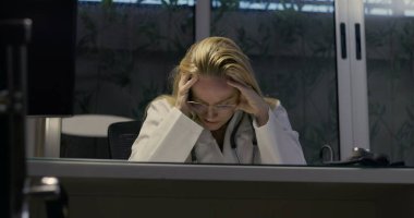 Kadın doktor umutsuzca başını eğiyor. Gece klinikte şiddetli yorgunluk belirtileri gösteriyor.