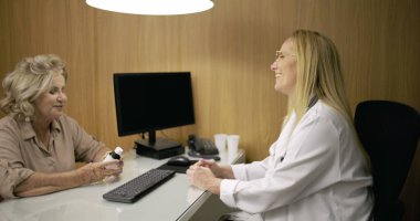 Üst düzey kadın, modern tıp bürosundaki dostane ve güven verici danışma sırasında kadın doktorla ilaç tartışırken gülümsüyor.