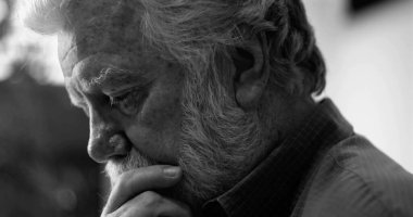 Derin düşüncelere sahip yaşlı bir adam çenesinin üzerinde dinleniyor, siyah ve beyaz yakın plan, duyguları ve iç mekanı sessiz bir anda ön plana çıkarıyor.