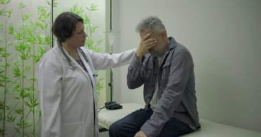 Orta yaşlı erkek hasta sinir bozucu teşhislere tepki verirken, kadın doktor klinik ortamda tıbbi konsültasyon sırasında duygusal destek sunuyor.