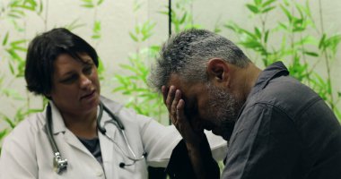 Kadın doktor, klinikte duygusal konuşmalar sırasında orta yaşlı bir erkek hastayla nazikçe konuşuyor ve omuz omuza destek veriyor.