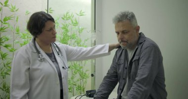 Klinikte tıbbi danışmanlık sırasında zor durumda olan orta yaşlı erkek hastaya destek veren kadın doktor