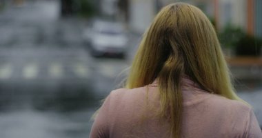 Yağmurda tek başına yürüyen bir kadın, arkadan görülüyor, sakin bir şehir sokağında yürüyor yalnızlık, yansıma ve duygusal ağırlık anında.