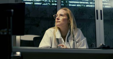 Gece vardiyası sırasında zor durumdaki kadın doktor, yoğun duygusal baskıyla karşı karşıya klinik ortamda otururken, ezici iş yükü ile boğuşurken,