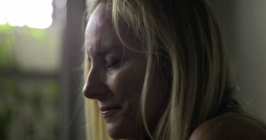 Kadın, sağlık hizmetleri çevresindeki bir anlık yansıma sırasında, gözleri kapalı, tek başına zor duyguları sindirerek sessizce tıbbi odada oturuyor.