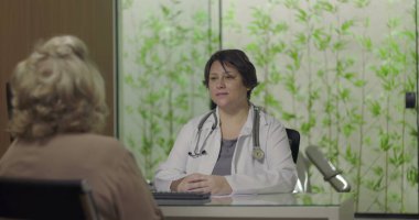 Steteskoplu doktor, klinikteki sağlık muayenesi sırasında yaşlı kadın hastayla konuşmaya odaklanmış.