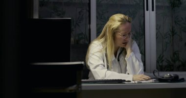 Masada el ele tutuşan kadın doktor geç saatlerde klinikte zihinsel ve fiziksel olarak yorgun görünüyor.