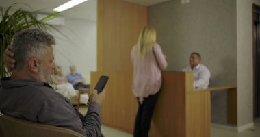 Kadın resepsiyonist ve doktorla konuşurken adam bekleme salonunda telefonu kontrol ediyor. Modern tıp kliniğinin lobisinde aktif bir an.