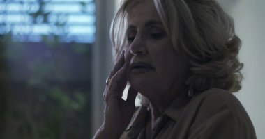 Duygusal yorgunluk ifadesiyle alnına dokunan yaşlı bir kadın ya da kapalı bir ortamda ezici bir stres.