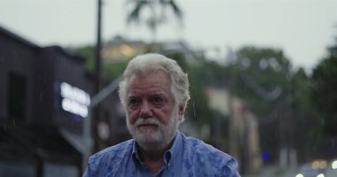 Kolları geniş ve yüzü göğe yükselmiş yaşlı bir adam, ruhsal rahatlama, minnettarlık veya duygusal teslimiyet ifadesiyle yağmuru kucaklıyor.