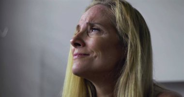 Duygusal bir anda gözleri kapatılan bir kadın, klinik ortamda keder ya da üzüntü ifade eden, yumuşak ışıklandırma, dışavurumundaki hassasiyeti ve gerilimi vurguluyor.