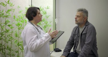 Klinik konsültasyonu sırasında erkek hastaya tıbbi bilgileri açıklamak için tablet kullanan doktor, açık iletişim ve hasta bağlarını vurguladı