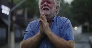 Yağmurun altında başıyla acı çeken yaşlı bir adam, gözleri kapalı, duygusal acı ve umutsuzlukla boğulmuş bir ifade.