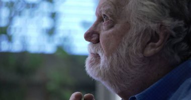Umudun ve yansımanın yumuşak ifadesiyle yukarı bakan yaşlı bir adam, yan profili çerçevelenmiş, kapalı arka planda nazik
