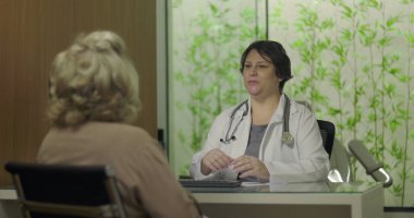 Steteskoplu gülümseyen doktor profesyonel klinikteki tıbbi danışmanlık sırasında yaşlı kadın hastayla samimi bir şekilde temas kuruyor.