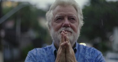 Yüzüne yapışmış elleri tutan yaşlı bir adam, yağmurda parlayan gözler, duygu, umut, ya da ruhsal bağlantı anında sessiz dua ile dolu.