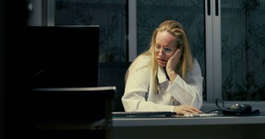 Kadın doktor gece geç saatlere kadar çalışırken masaya yaslanıyor. Yorgun ve bitkin görünüyor.