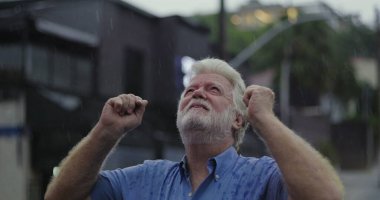 Yağmurun altında başıyla acı çeken yaşlı bir adam, gözleri kapalı, duygusal acı ve umutsuzlukla boğulmuş bir ifade.