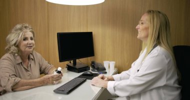 Üst düzey kadın, modern tıp bürosundaki dostane ve güven verici danışma sırasında kadın doktorla ilaç tartışırken gülümsüyor.